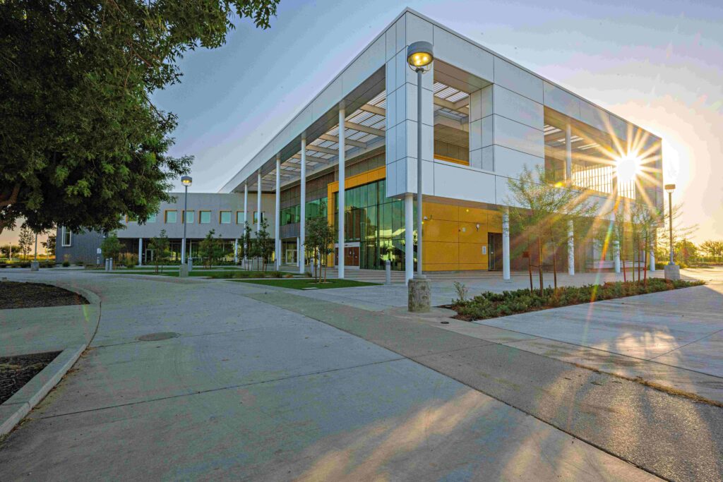 Modern two-story building with large windows and a sun flare at the corner, surrounded by trees, streetlights, and a paved walkway.